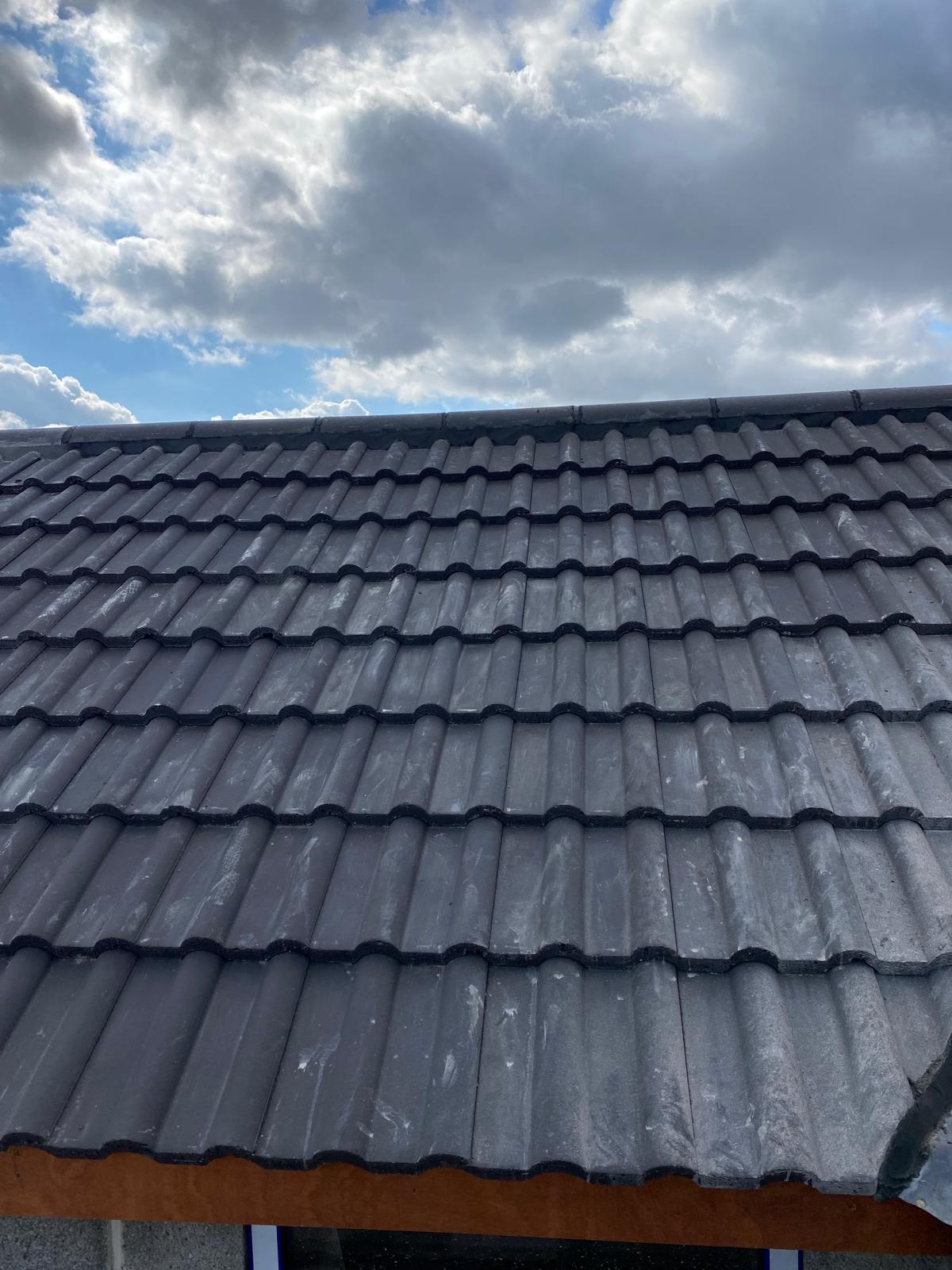 New grey pitched roof tiles freshly laid against blue sky &mdash; UK re-roof project